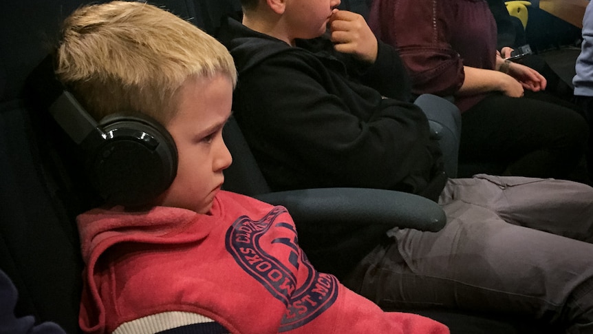 A boy wears headphones while seated in a theatre with other people.