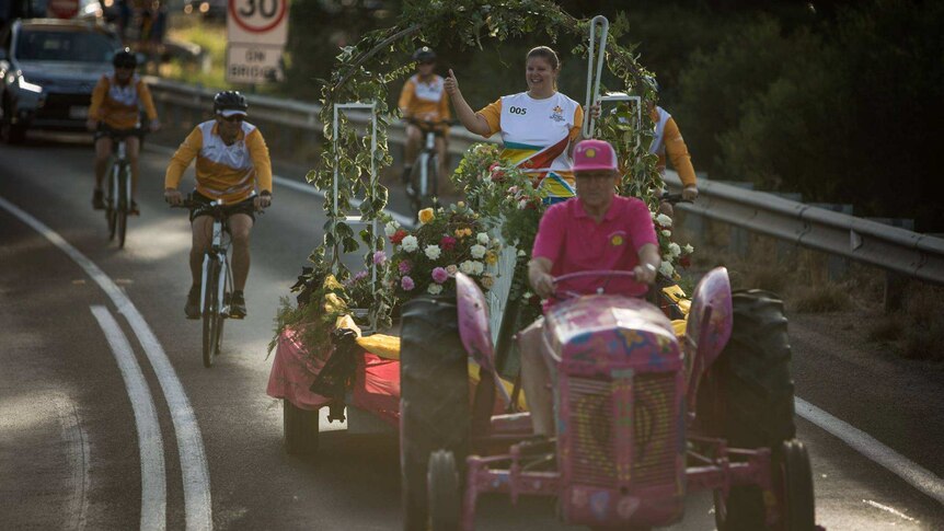 A woman carries the Queen's Baton on the back of a tractor decorated with roses.