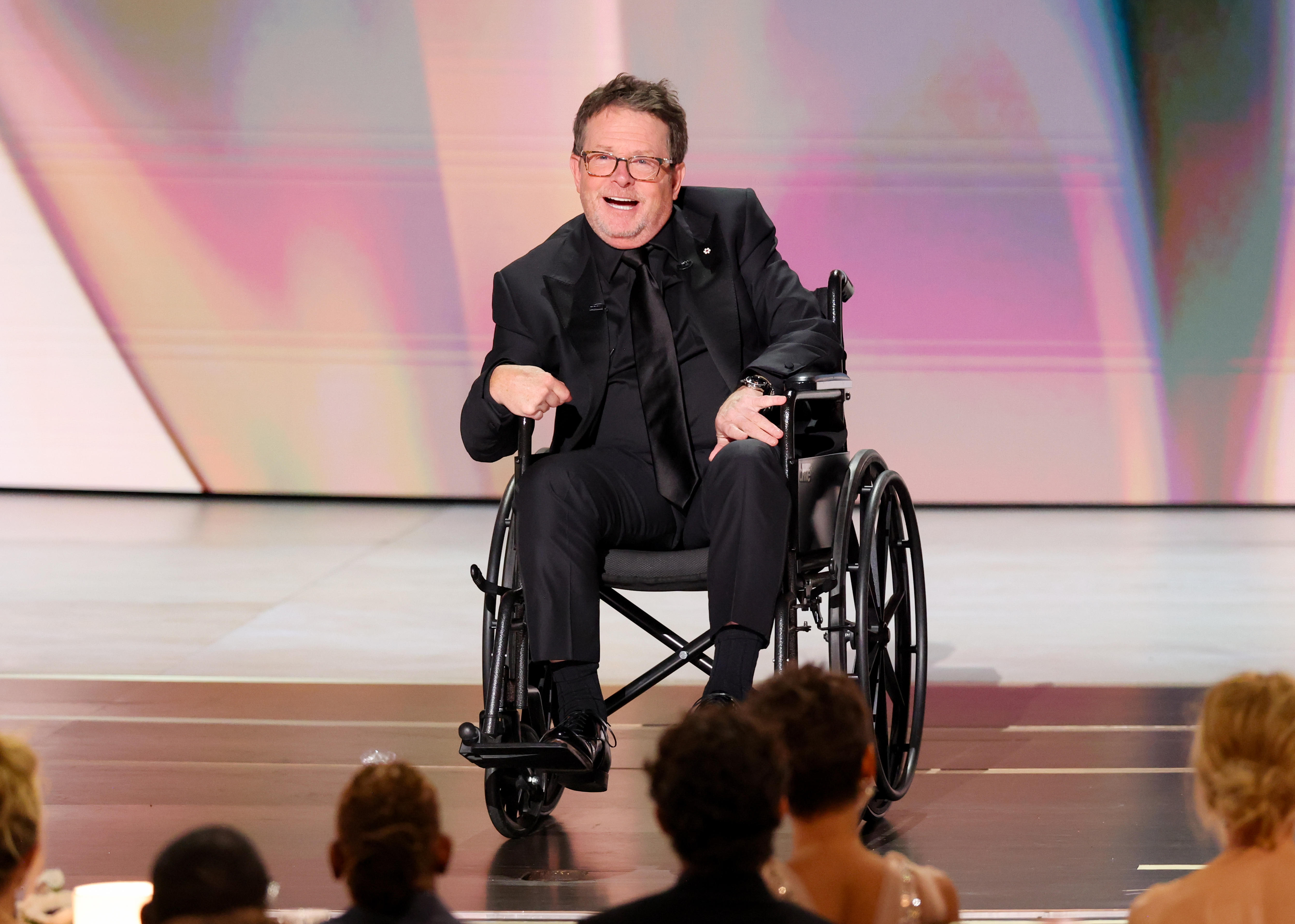 A man in a wheelchair on a stage smiles at the audience