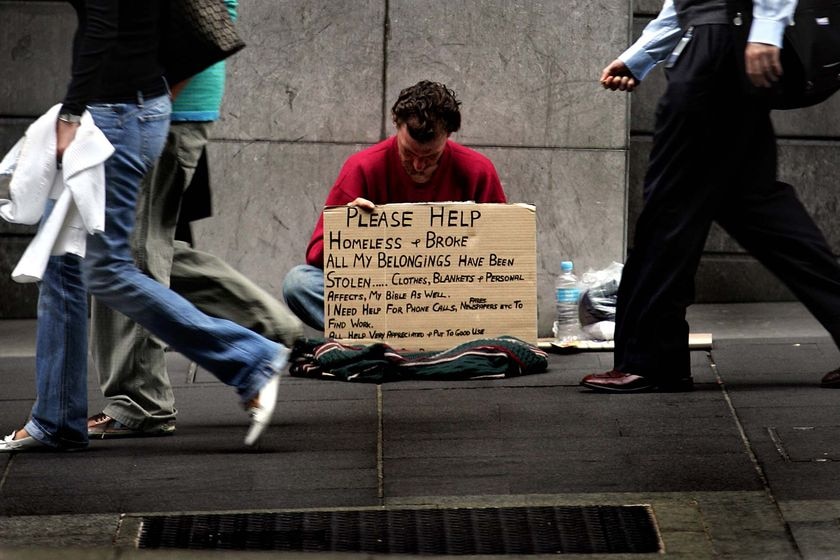 A homeless man begs for money as pedestrians walk past
