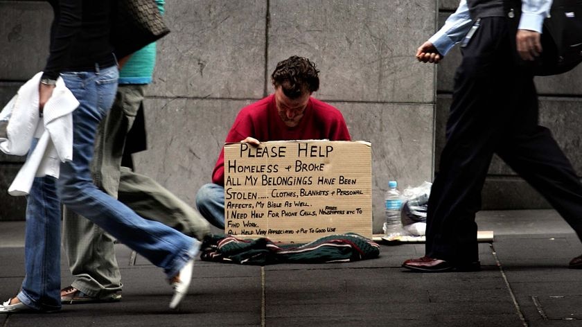 A homeless man begs for money as pedestrians walk past