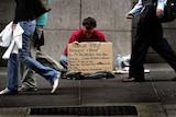 A homeless man begs for money as pedestrians walk past