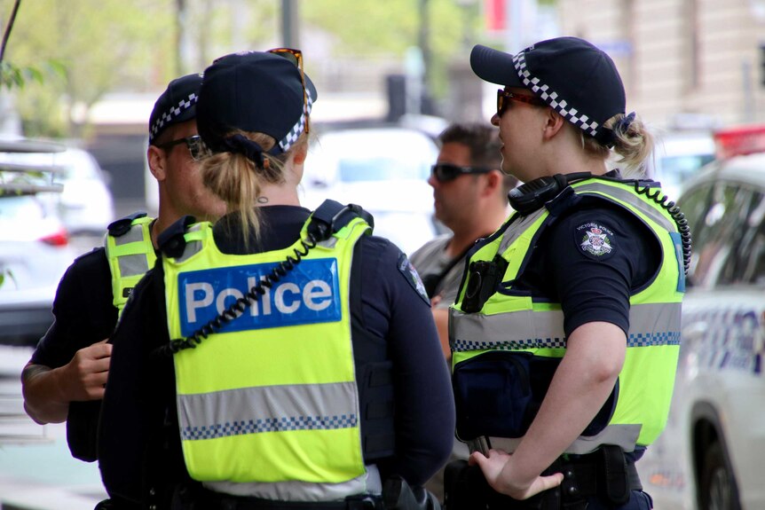 Three police officers talk on a Melbourne street.
