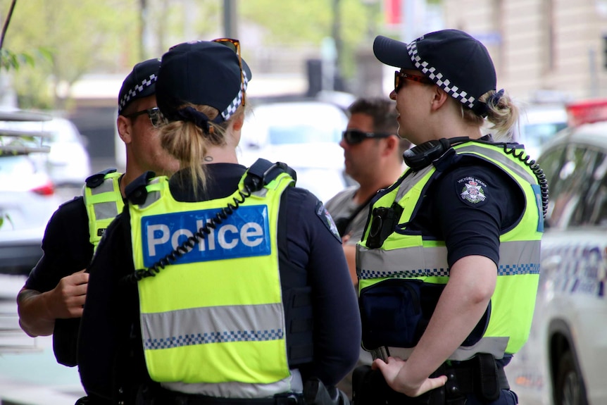 Three police officers talk on a Melbourne street.