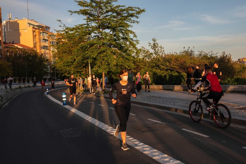 People jog through a park wearing face masks.