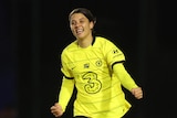 sam kerr runs on field wearing bright yellow long sleeve strip smiling