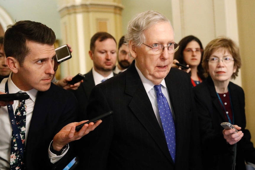 A group of journalists holding mobile phones surround Senate Majority Leader Mitch McConnell in the halls of the US Senate.