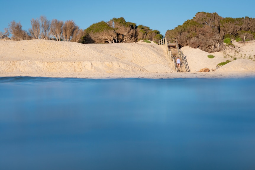 A woman walks up a set of beach stairs.