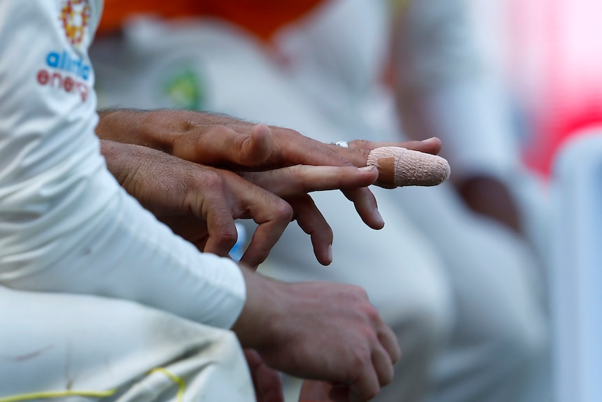 A close-up shot of a cricketer's hand, with the middle finger heavily bandaged, as a coach examines it with his finger.