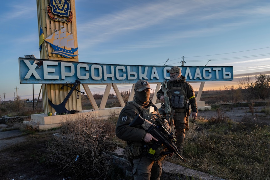 Two soldiers in front of a sign which reads "Kherson region"