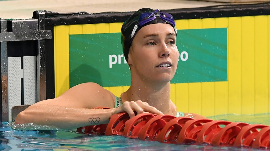 Woman in black cap rests at end of swimming pool