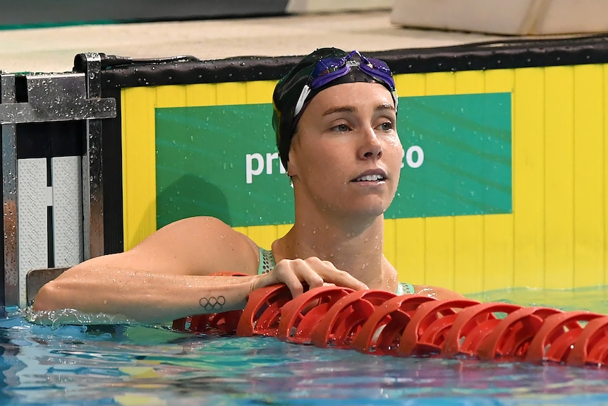 Woman in black cap rests at end of swimming pool