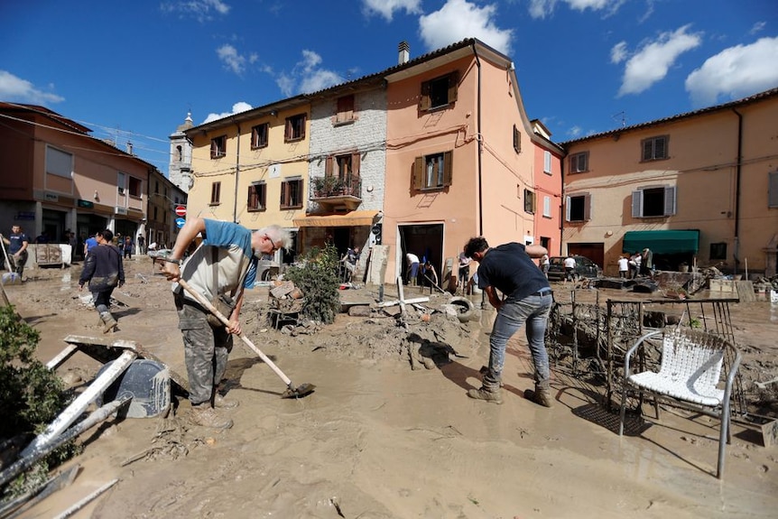 People stand in mud after deadly flooding cleaning up. 