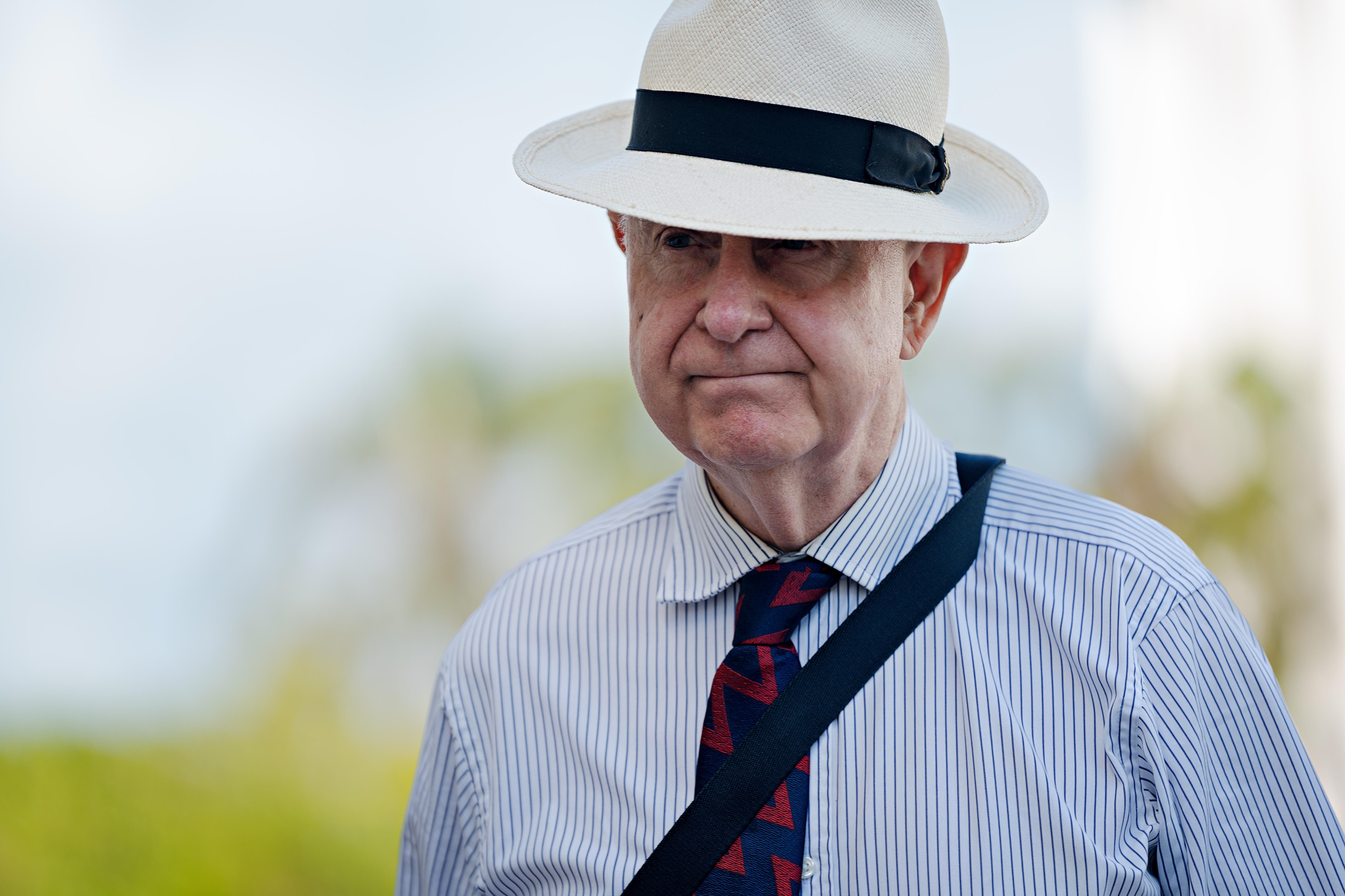 Un hombre con sombrero y vestido de negocios camina afuera en un día soleado.