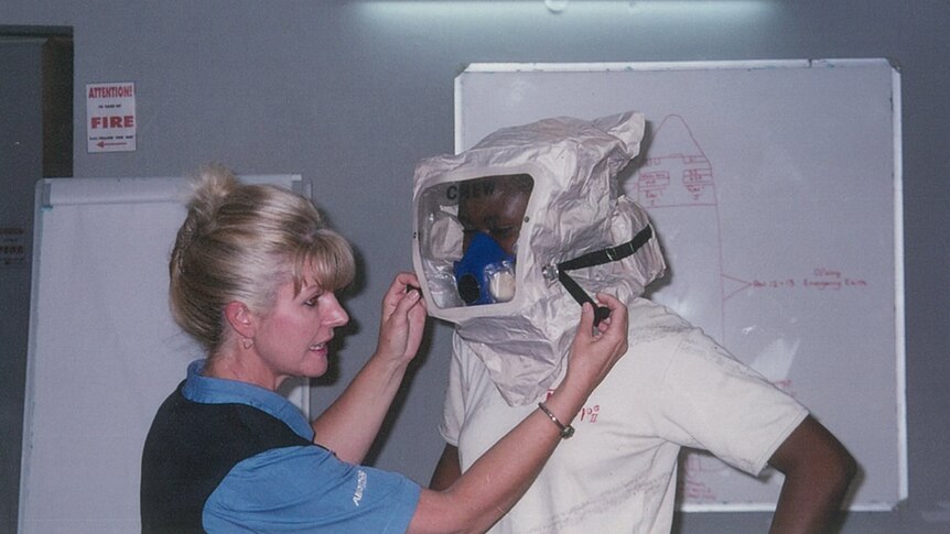 A blonde woman stands next to a tall elegant African woman who has a fire safety mask on.