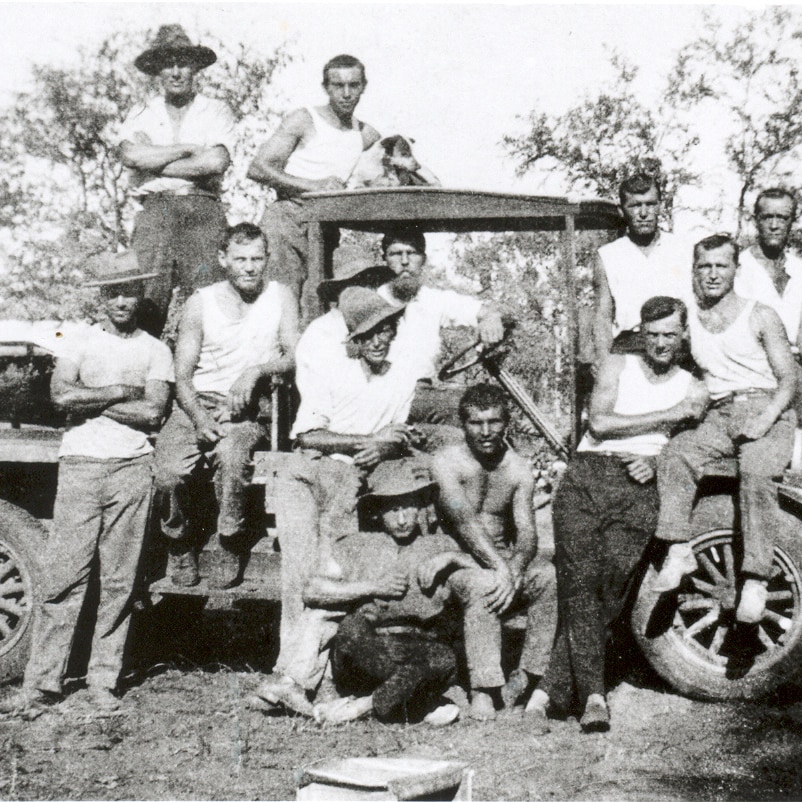 A group of Russian men and women are sitting on a tractor in a historical photo