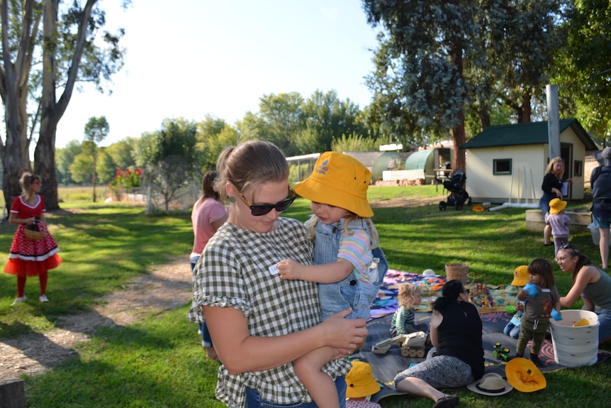 A woman holds a little girl while children play in the background