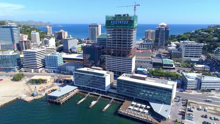 A tall tower being constructed in the middle of an city with ocean in the background