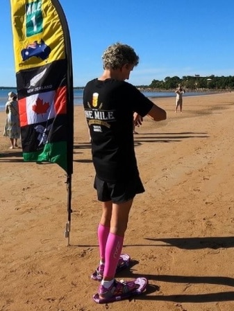 A man on a beach in the afternoon poised to start running in snowshoes beside a flag.