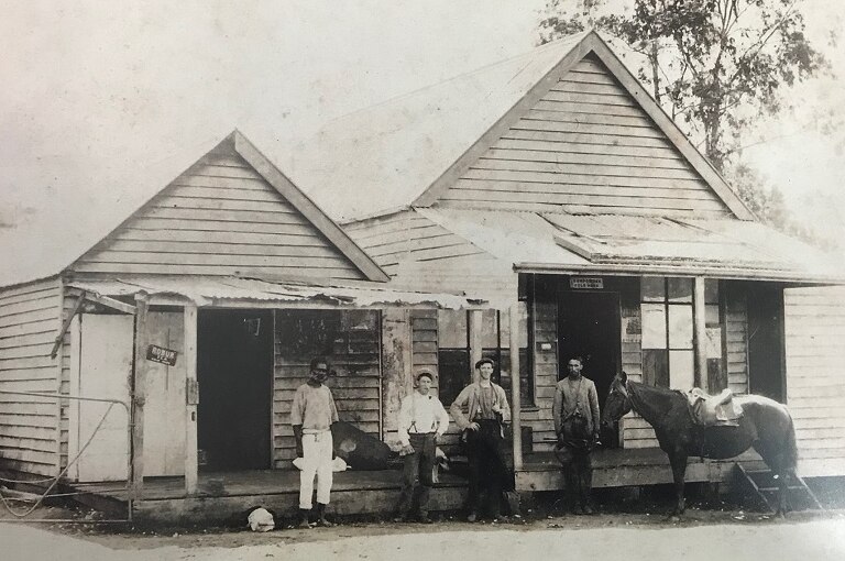 An historic black and white photo of an old building with four men and a horse standing outside the front of it.