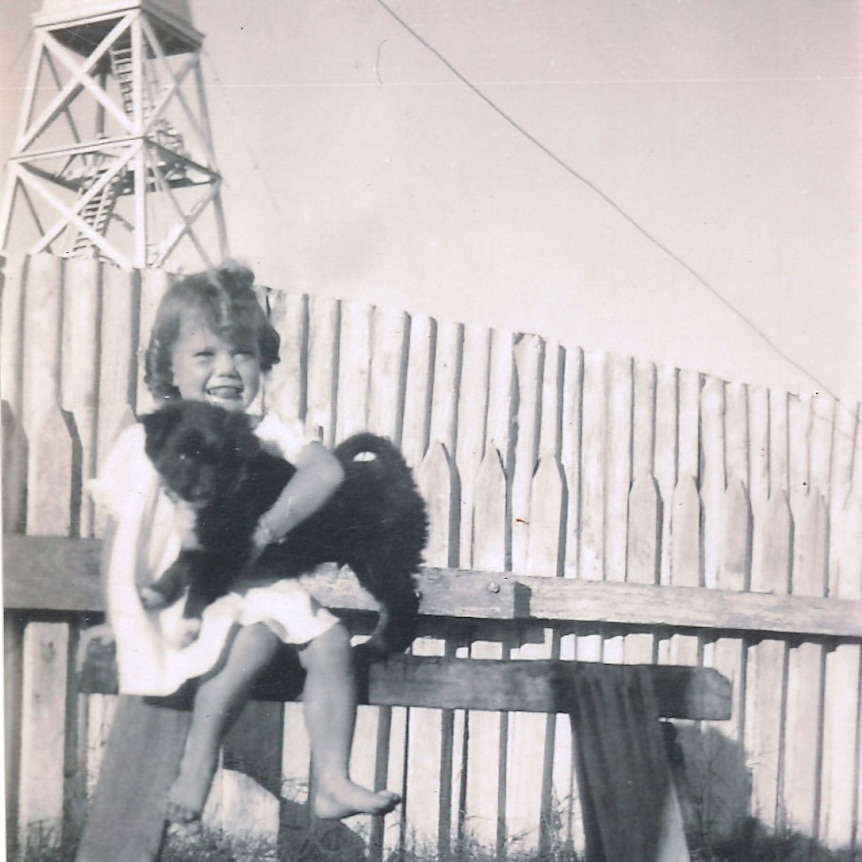 A black and white photo of a girl holding a dog in front of a tower structure.