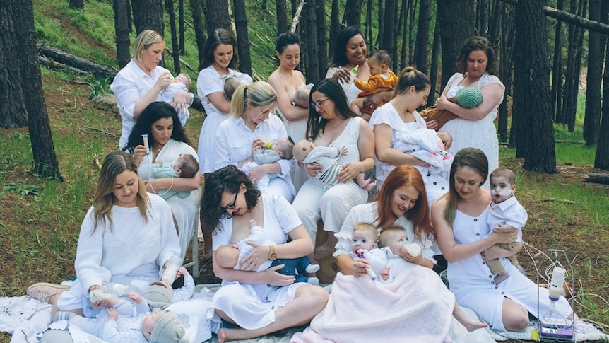 A group of women wearing white and sitting in a forest among trees holding babies