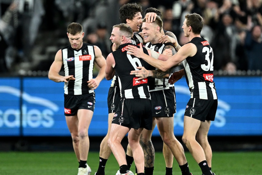 Un groupe de joueurs de Collingwood AFL s'embrassent et célèbrent après un but.