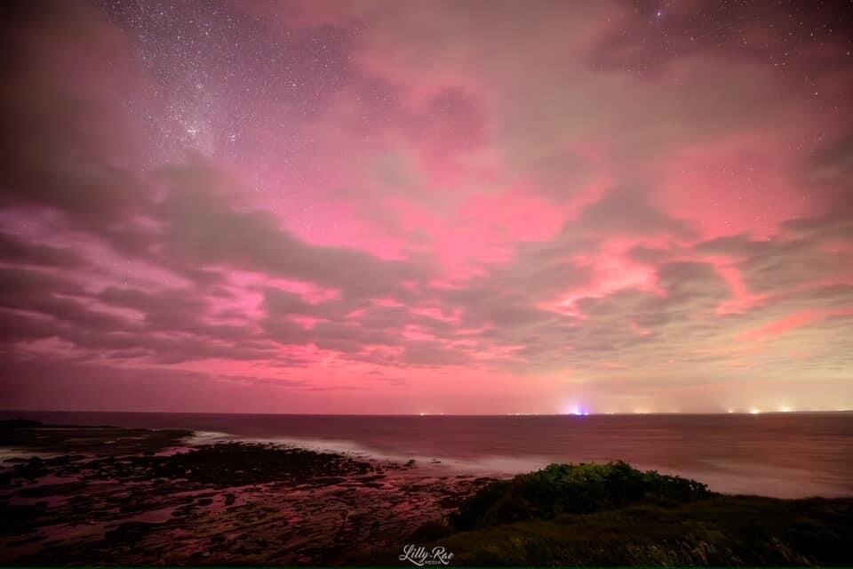 A pink aurora in the night sky with the ocean in the background