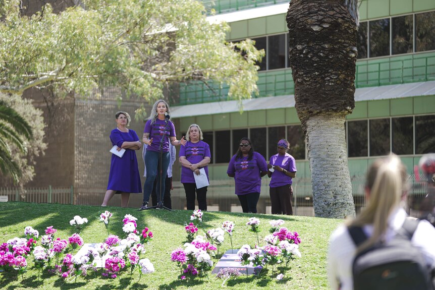 a group of women standing near flowers wearing purple