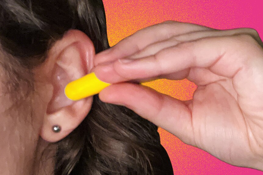 A woman puts a foam earplug into her ear.