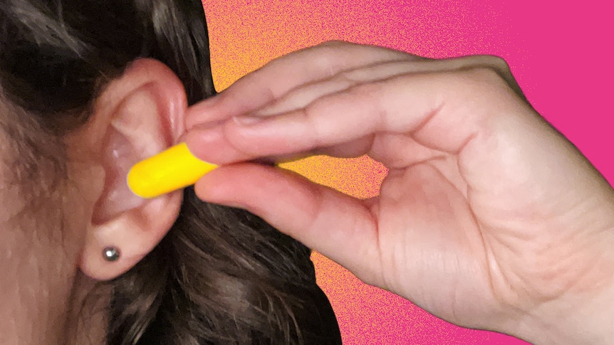 A woman puts a foam earplug into her ear.