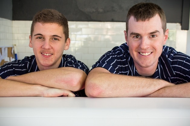 Two men wearing butcher's shirts lean on a shop counter