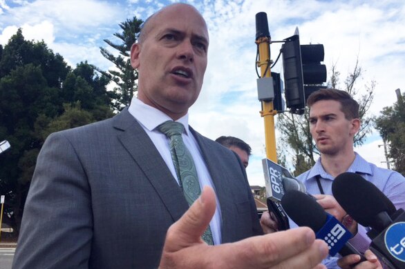Dean Nalder speaks to reporters holding microphones in front of a set of traffic lights in Karrinyup.