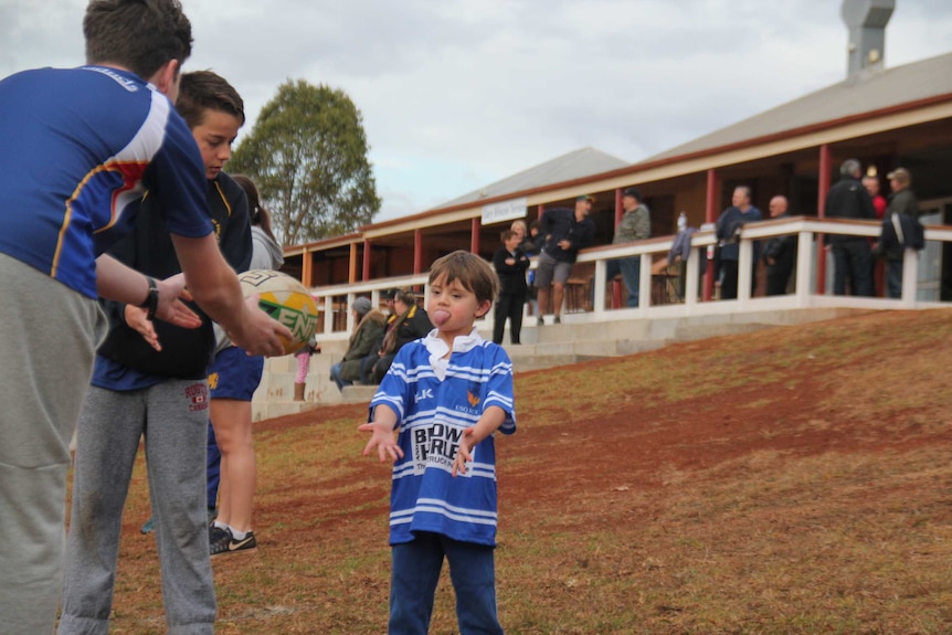 Young boy playing with football on sports oval with two teenage boys.