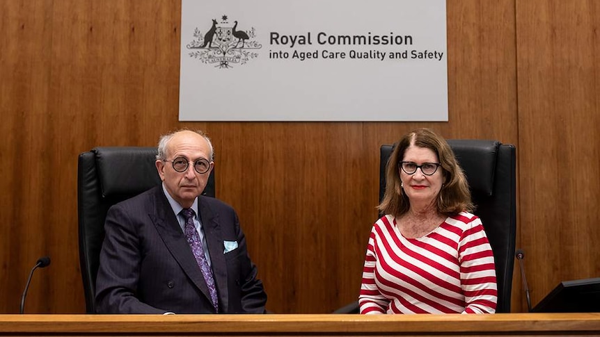 A man and a woman sit in front of the royal commission signage.