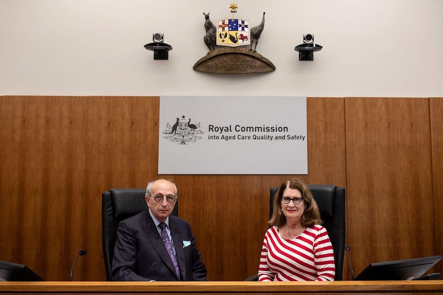 A man and a woman sit in front of the royal commission signage.