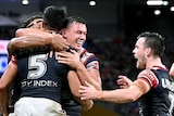A group of rugby league players celebrate a try as an opposition player looks on