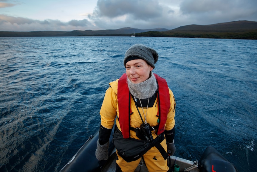 Woman on bow of boat looking back, with ocean and land in background