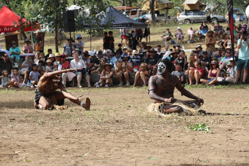 AN Aboriginal man moves his hands like a crocodile in a dance performance, locking his gaze on another dancer.