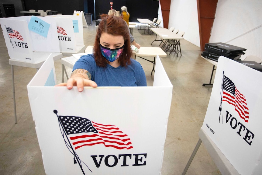 A woman stands at a booth that reads VOTE