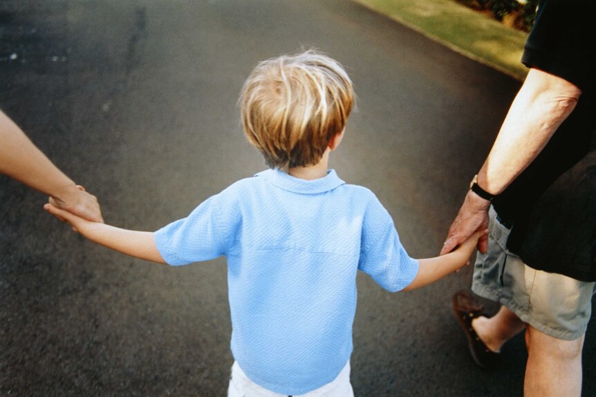 A boy walks between his parents, holding each of their hands.