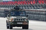 Xi Jinping inspects perfectly lined-up soldiers, tanks and red flags in Hong Kong. He is standing in the back of an army jeep.