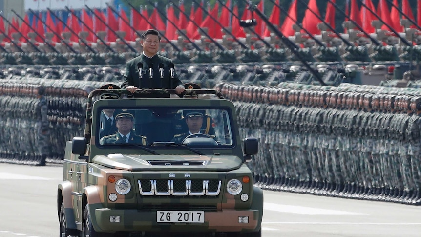 Xi Jinping inspects perfectly lined-up soldiers, tanks and red flags in Hong Kong. He is standing in the back of an army jeep.