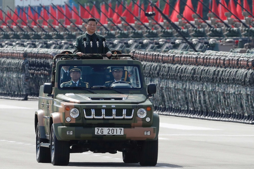 Xi Jinping inspects perfectly lined-up soldiers, tanks and red flags in Hong Kong. He is standing in the back of an army jeep.