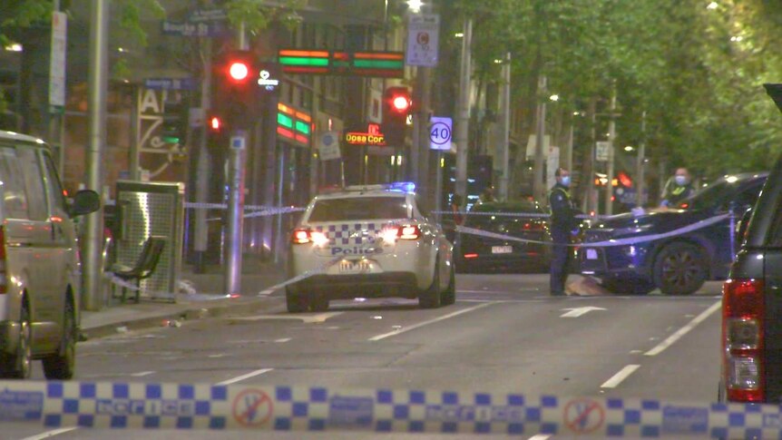 Police officers and cars behind crime scene tape on a Melbourne CBD intersection at night-time.