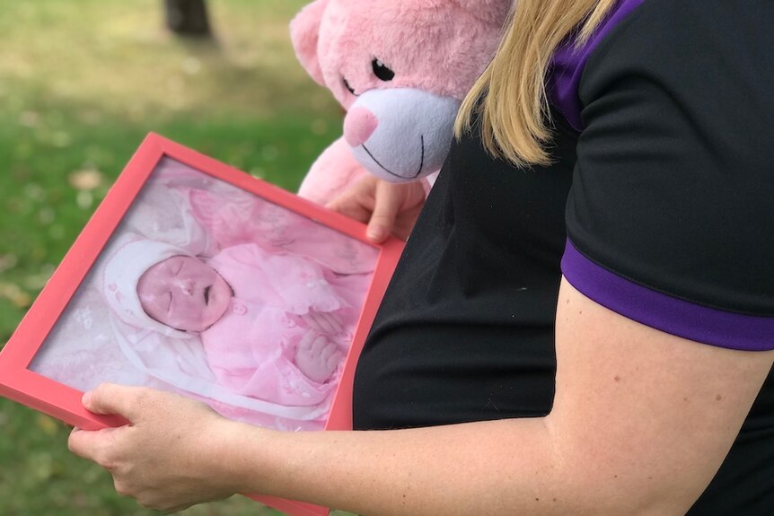 A pregnant woman holds a photograph of her stillborn baby and a pink teddy bear.