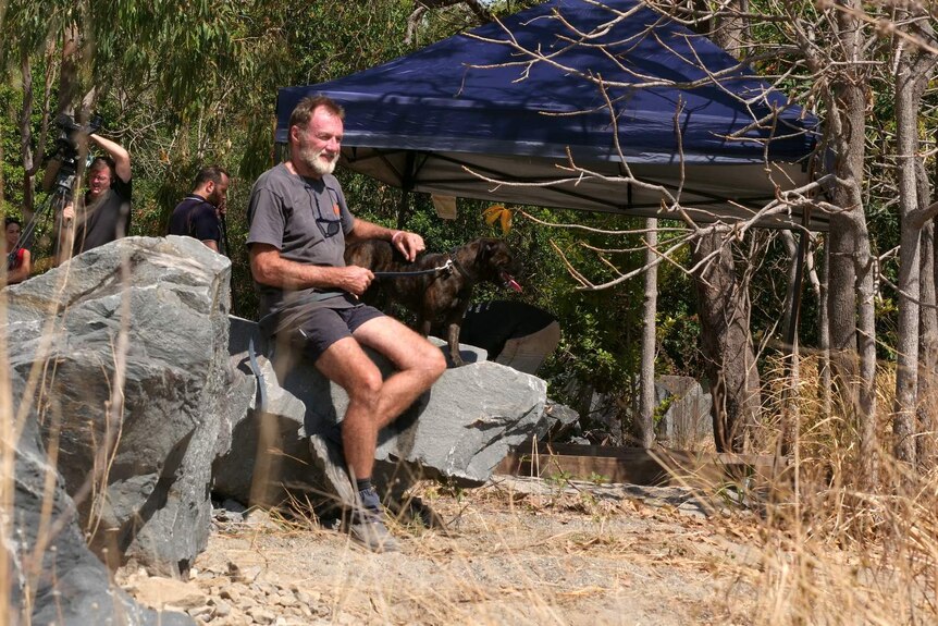 Wayne Trimble sits on a rock with his dog.