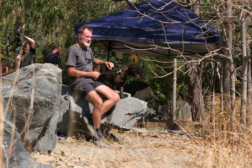 Wayne Trimble sits on a rock with his dog.