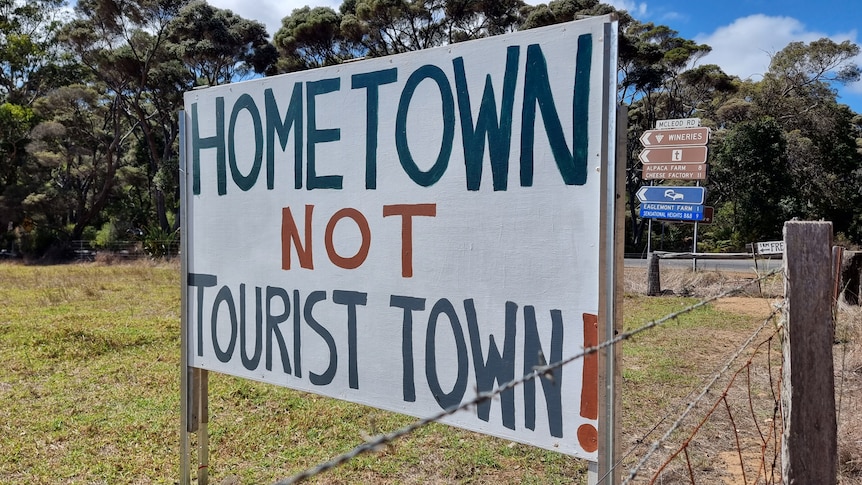 A white sign saying "Hometown not tourist town" on a green field.