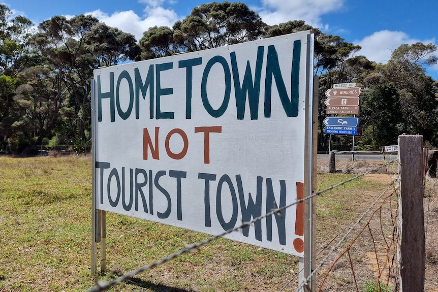 A white sign saying "Hometown not tourist town" on a green field.